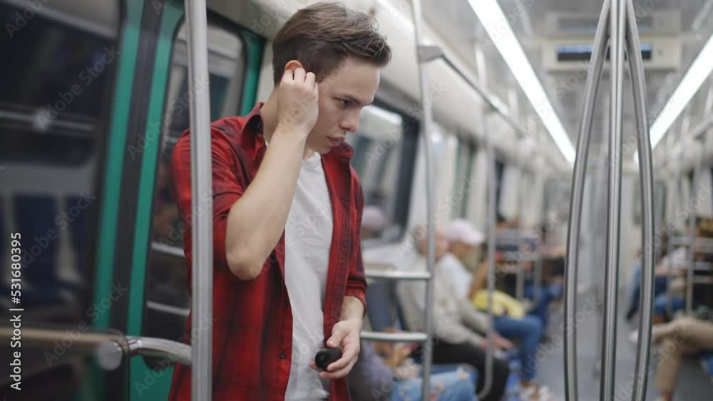 A young man in a plaid shirt rides standing in the subway, puts on wireless headphones, moves his head to the beat of the music. Slow motion 120fps footage A young man in a plaid shirt rides standing in the subway, puts on wireless headphones, moves his head to the beat of the music. Slow motion 120fps footage