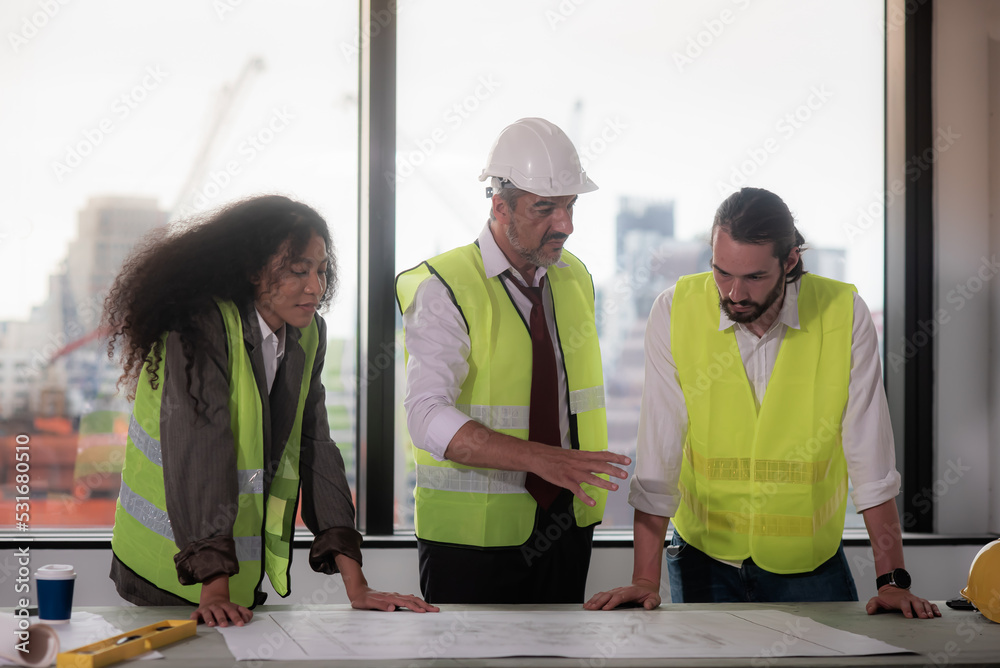 Senior caucasian Project manager Wearing white shirt and tie with safety workwear, Discussing with the team to up to date progress of building construction Compare with plans in the project blueprint.