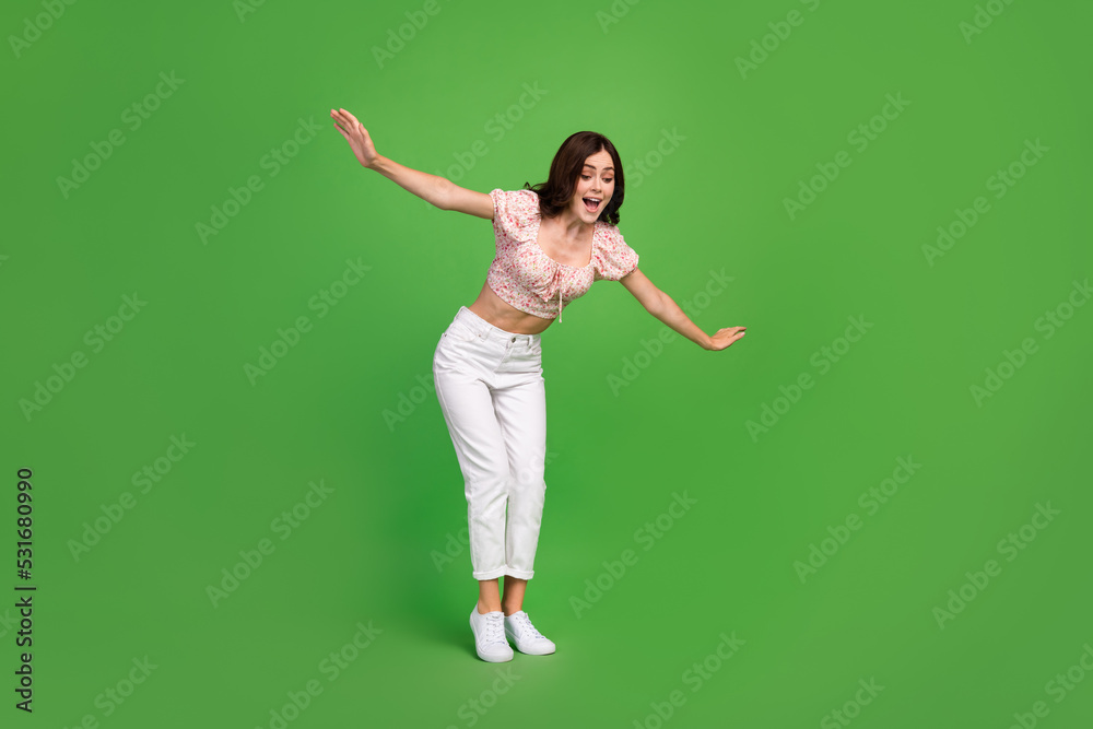 Full length photo of pretty woman with curly hairdo wear white trousers blouse look down hold balance isolated on green color background Full length photo of pretty woman with curly hairdo wear white trousers blouse look down hold balance isolated on green color background