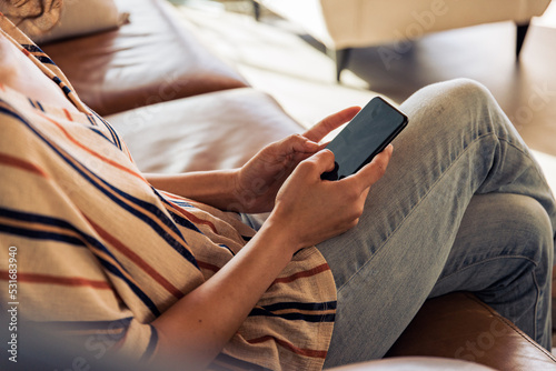 Businesswoman sitting on sofa at home using mobile phone. Woman working on mobile phone at home and managing her business.