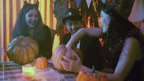 Two girls and a guy in creepy Halloween costumes are sitting at a table and taking the pulp out of pumpkins