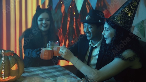 A group of friends celebrate Halloween and drink juice at the table from glasses in the form of a pumpkin