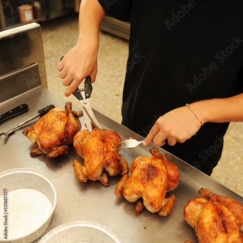 Carving the roasted chickens on the chicken spit. Chicken rotisserie employee preparing chickens for serving orders