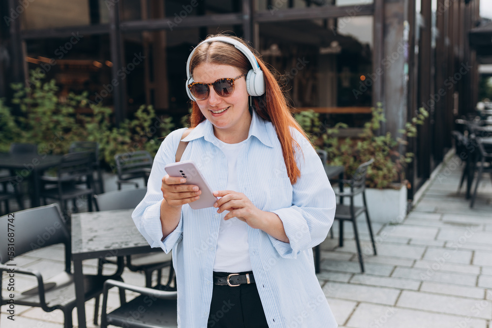 Close up portrait of a lovely happy young woman listening to music through wireless earphones on urban background. Music lover enjoying music. Lifestyle concept.