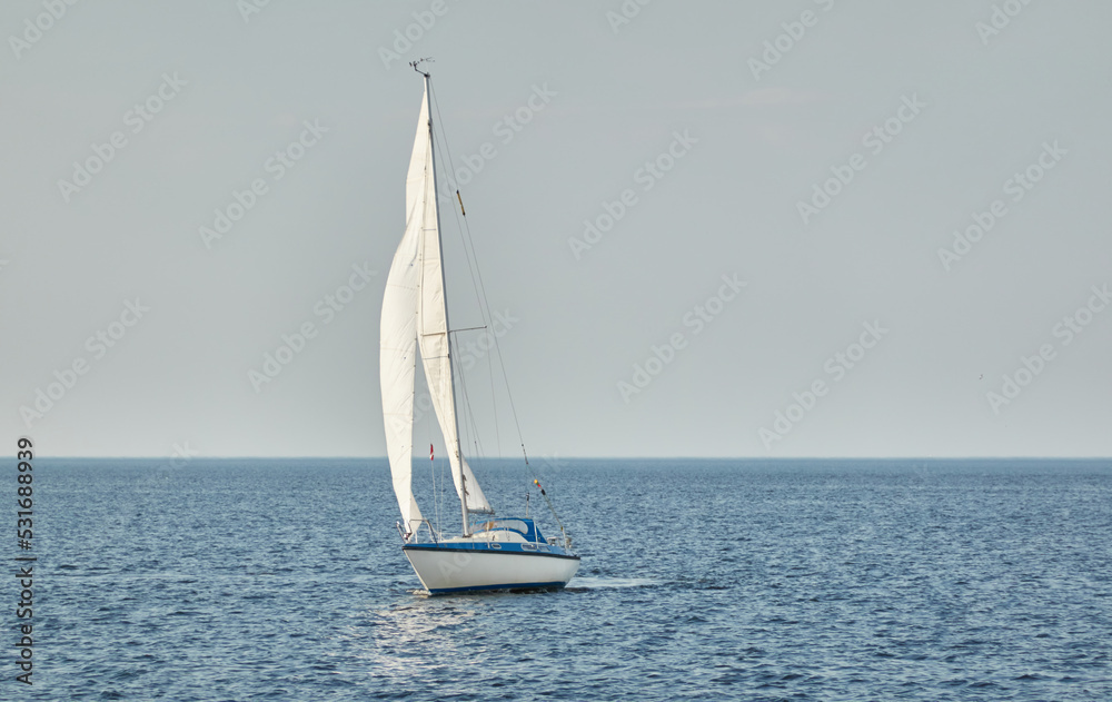 Obraz premium White sloop rigged yacht sailing in the Baltic sea on a clear day. Transportation, cruise, yachting, regatta, sport, recreation themes. Travel, exploring, wanderlust concepts