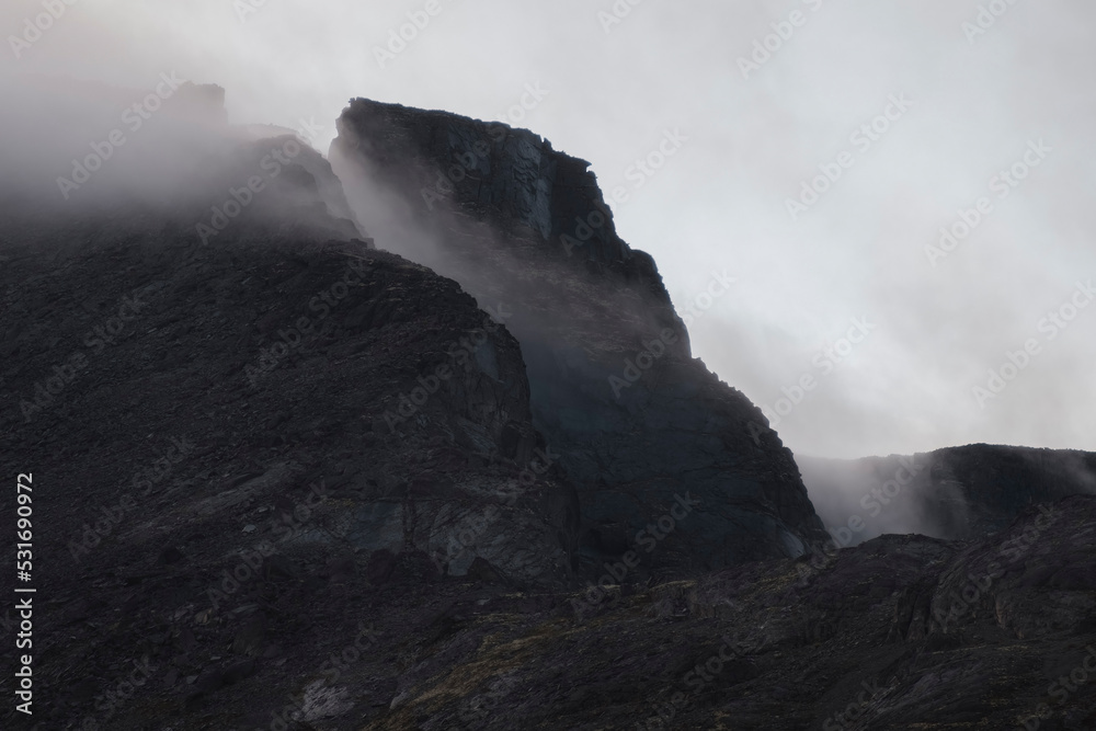 Harsh stone rocks in the clouds and fog in black mountains.