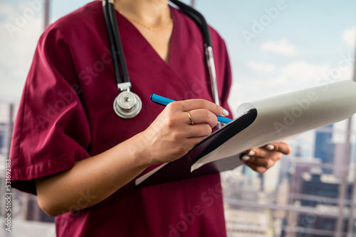 Cropped image of nurse holding folder with documents in hallway of main hospital.