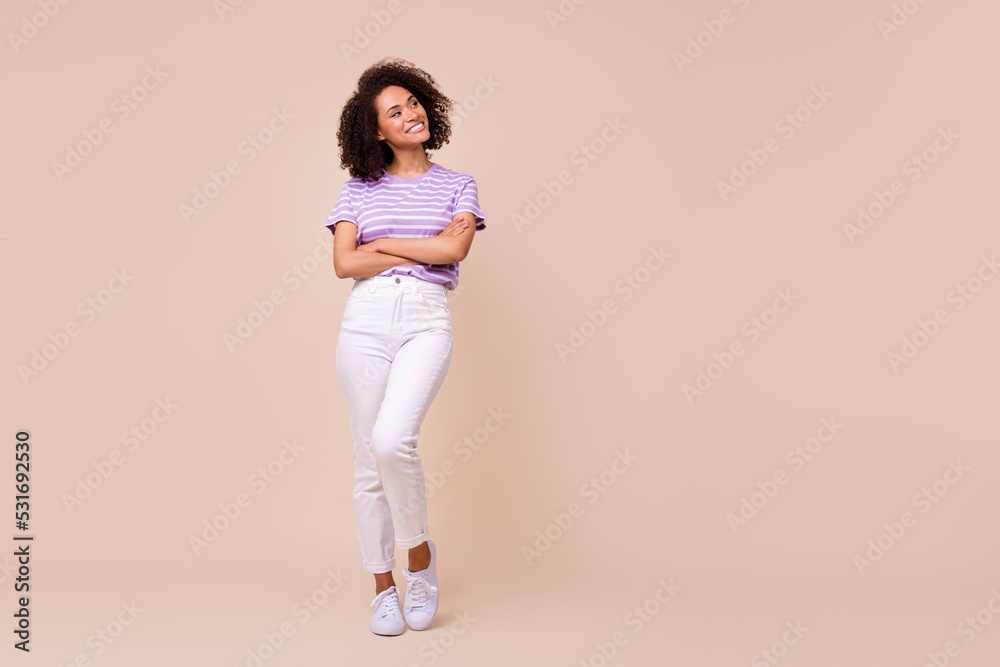 Full body size photo of young adorable woman crossed hands look empty space interested information ad isolated on beige color background Full body size photo of young adorable woman crossed hands look empty space interested information ad isolated on beige color background