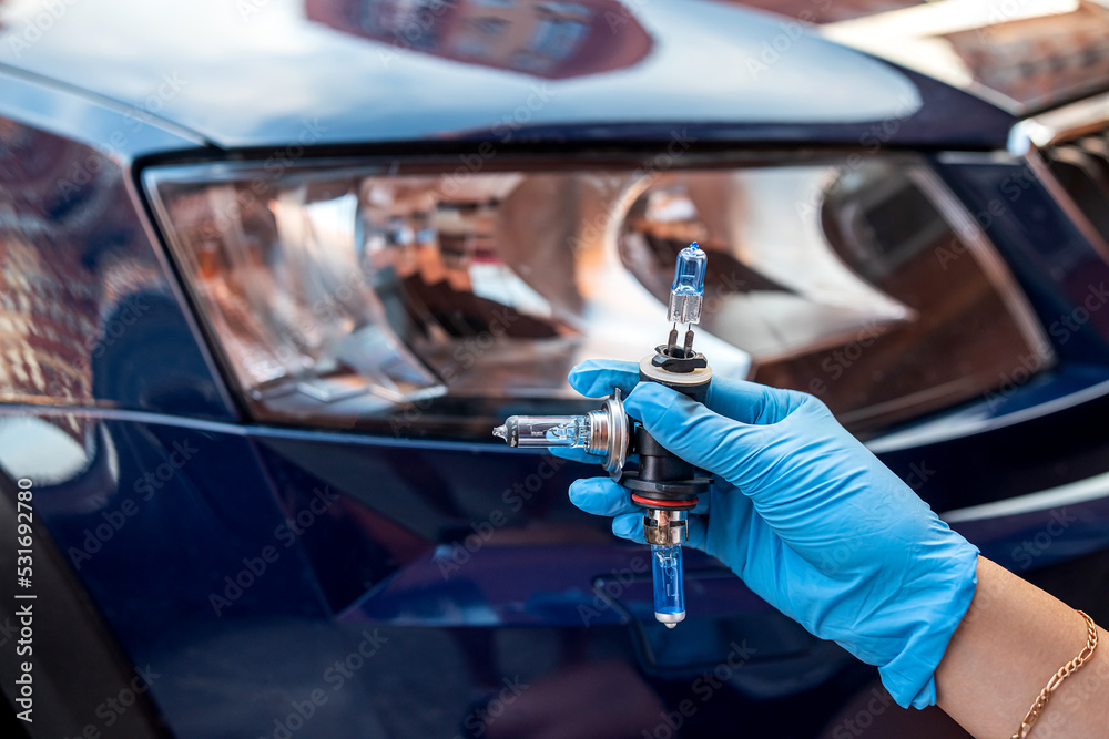 halogen bulb in a man's hand against the background of the headlights of a beautiful car