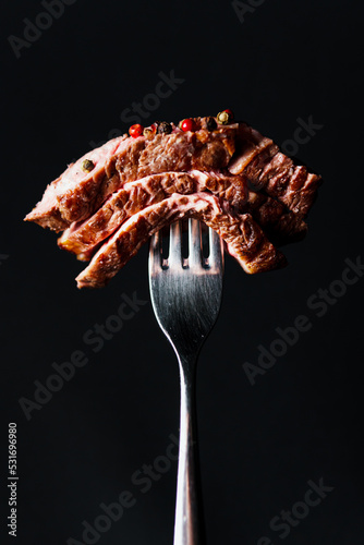 Sliced grilled steak medium rare on the fork, close up, black background. Delicious juicy meat in the restaurant menu. Concept of catering