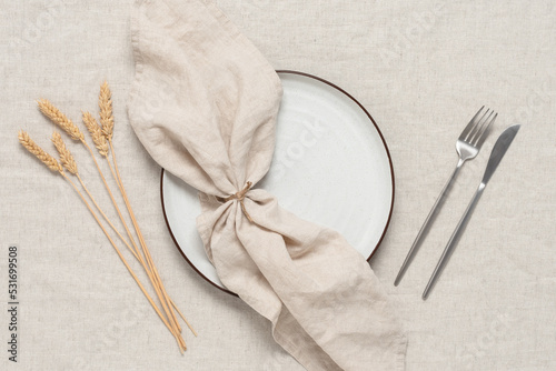 Autumn minimal table setting with ripe ears of wheat on a beige linen textile background. View from above.