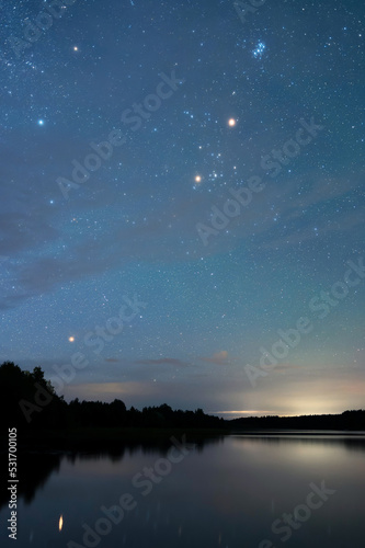 Autumn night landscape under starry sky. Stars reflecting from calm water surface.