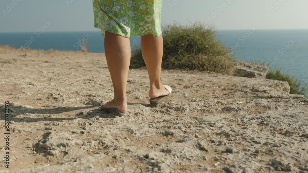 A girl in a green dress walks along the edge of a cliff, a cliff into the sea. Following.