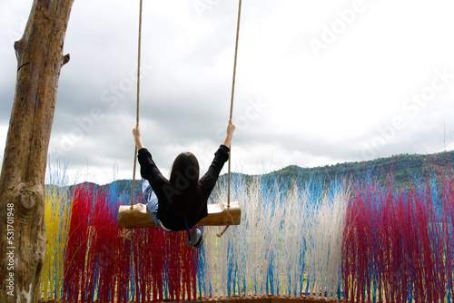 Back of Asia girl in black playing swing with the clouds sky and colorful dry tree from Thailand.