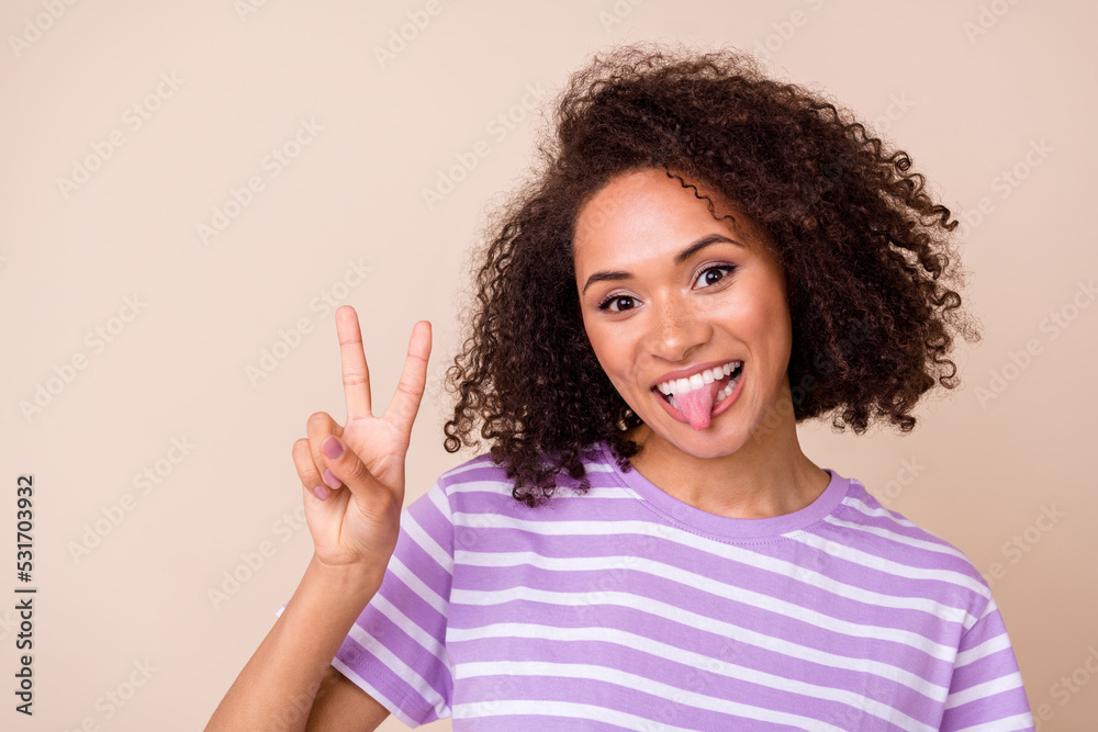 Photo of pretty shiny girl dressed purple t-shirt showing v-sign tongue out isolated beige color background Photo of pretty shiny girl dressed purple t-shirt showing v-sign tongue out isolated beige color background