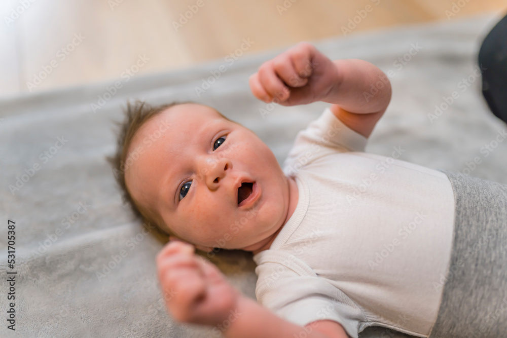 Indoor closeup portrait of a little infant baby boy clenching his fists and yawning with open mouth and eyes. Dark thin hair. Blurred background. High quality photo Indoor closeup portrait of a little infant baby boy clenching his fists and yawning with open mouth and eyes. Dark thin hair. Blurred background. High quality photo
