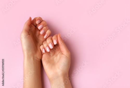 Female hands with natural beautiful manicure on pink background. Nude nail polish. Cosmetics, beauty, self care concept. Top view