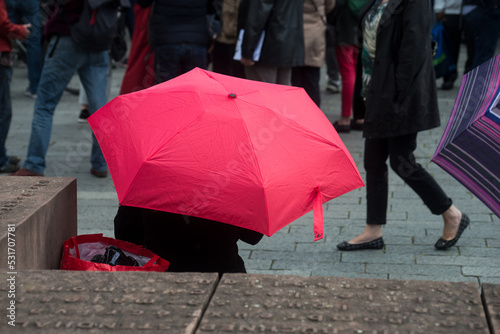 Portrait on back view of young woman sitting in the street with a red umbrella
