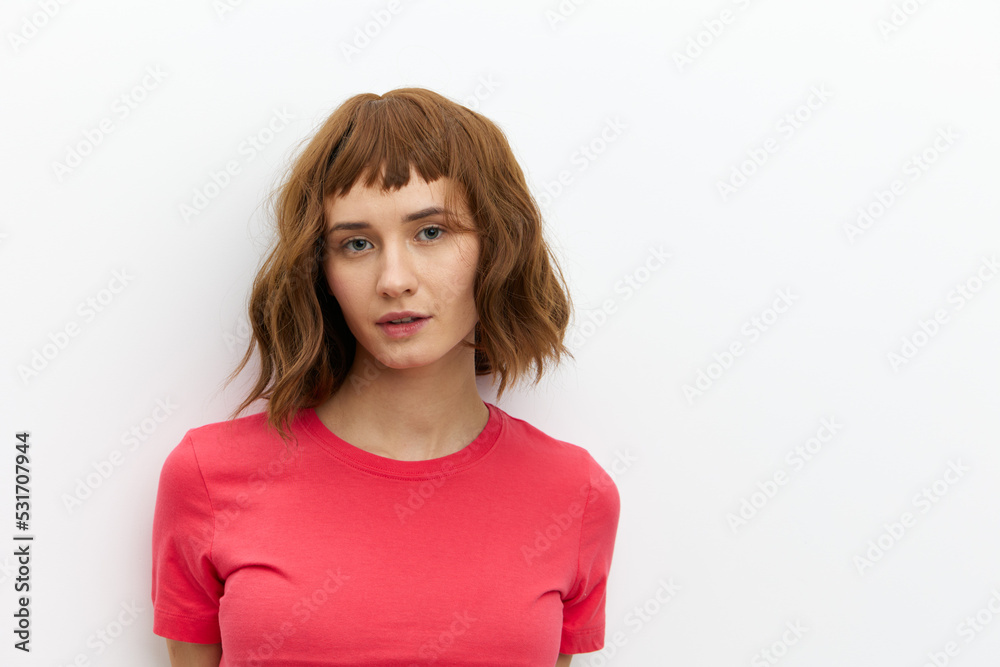 a close, horizontal portrait of a beautiful, attractive woman with short red hair standing in a red T-shirt and looking into the camera with a calm expression on her face. a close, horizontal portrait of a beautiful, attractive woman with short red hair standing in a red T-shirt and looking into the camera with a calm expression on her face.
