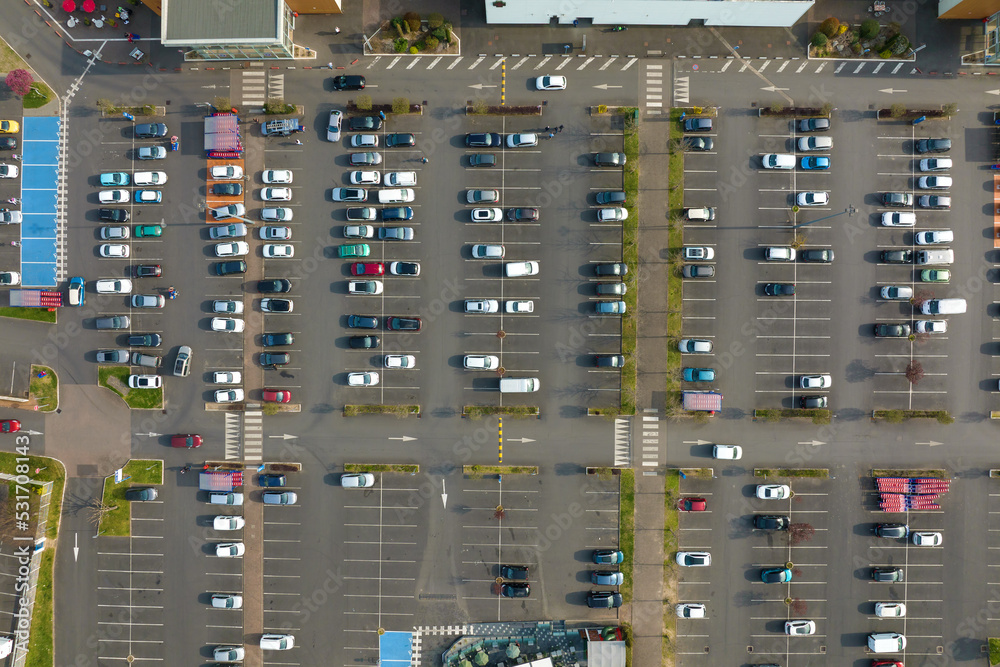 Aerial view of many colorful cars parked on parking lot with lines and markings for parking places and directions