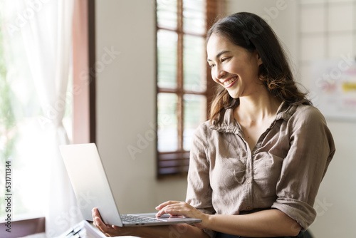 Asian thai businesswoman using laptop at working desk in modern office, busy job but feeling happy. © NanSan