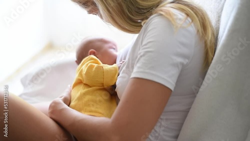 Mother-blonde in white T-shirt holds baby in yellow overall on hands and breastfeeds. Newborn - happiness for family. New worries and lifestyle.