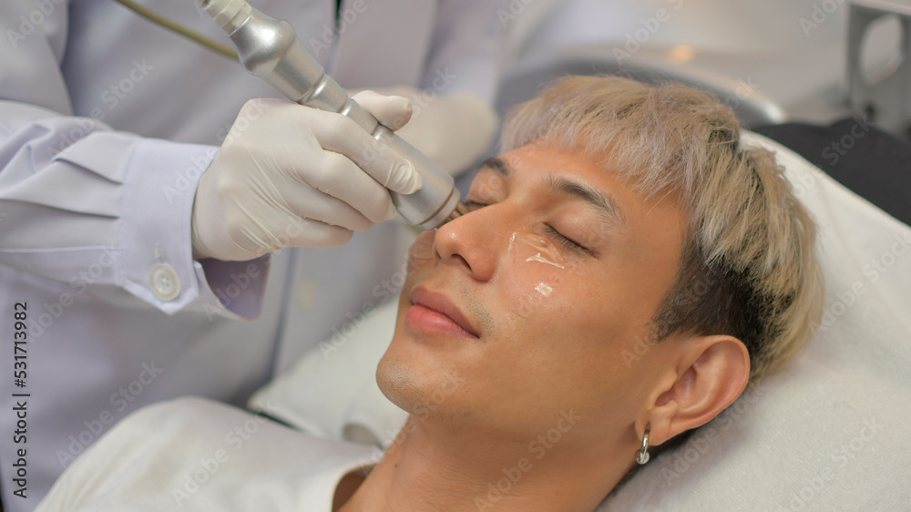 A handsome Asian man undergoes facial rejuvenation in a beauty clinic using modern medical equipment. By certified beauty experts according to standards.