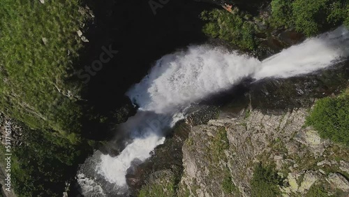 AERIAL: Slow motion of a powerful stream of a mountain waterfall photo