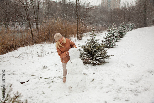 Woman makes a snowman in a city park during a snowfall