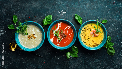 A set of colored soups. Tomato soup, pumpkin and mushroom soup. In a blue plate. On a black stone background. photo