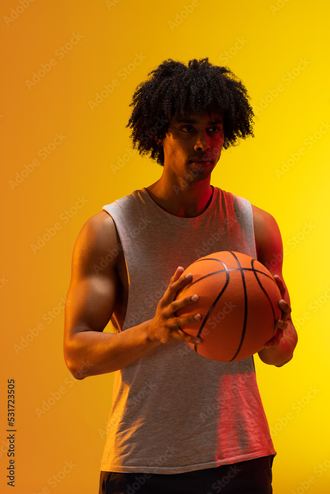 Image of biracial basketball player with basketball on orange to yellow background Image of biracial basketball player with basketball on orange to yellow background
