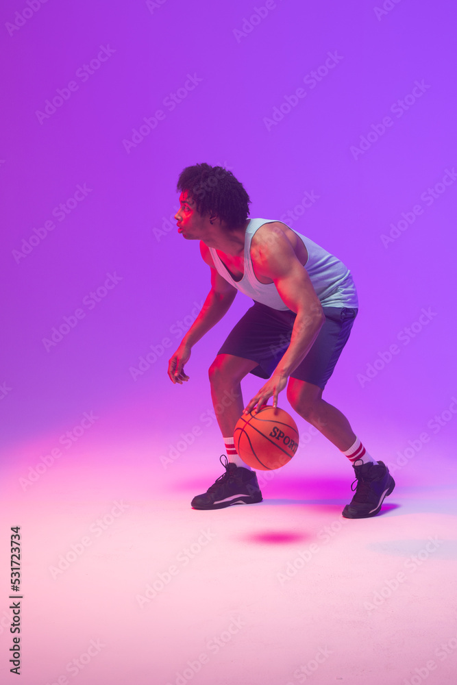 Image of biracial basketball player bouncing basketball on neon purple background
