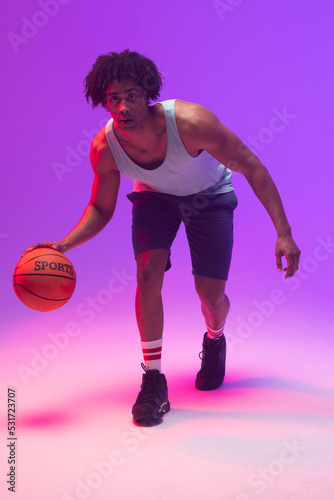 Image of biracial basketball player bouncing basketball on neon purple background