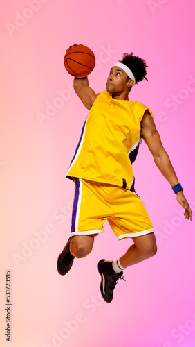 Image of biracial basketball player jumping in the air with basketball on pink background