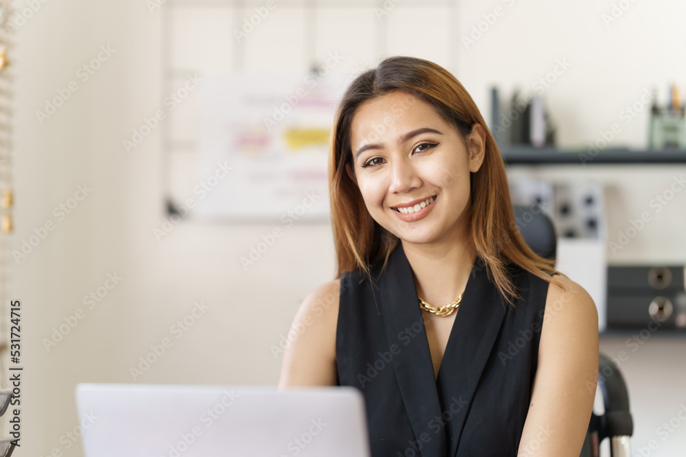 Looking camera, Asian thai businesswoman using laptop at working desk in modern office, busy job but feeling happy. Looking camera, Asian thai businesswoman using laptop at working desk in modern office, busy job but feeling happy.