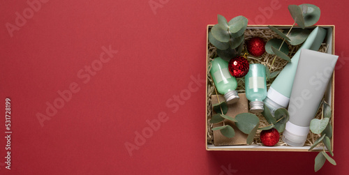 Beauty box with face and body care products on red background. Tubes with cream and lotion, soap, eucalyptus leaves. Organic cosmetics gift