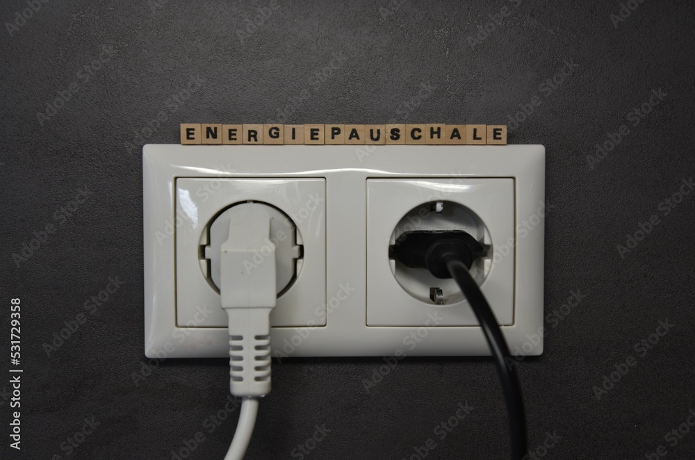 Das Wort Energiepauschale über einer Steckdose an der Wand Das Wort Energiepauschale über einer Steckdose an der Wand