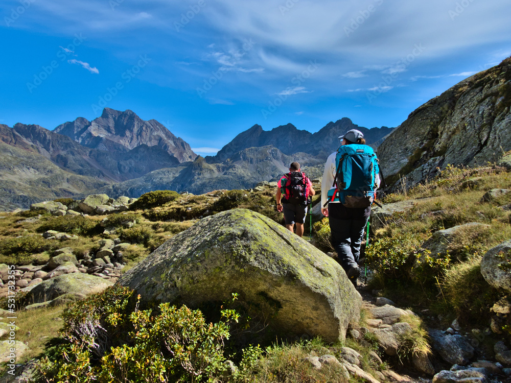 Alpine mountain landscape with couple, man and woman, trekking or hiking behind a stone with blue sky with clouds.