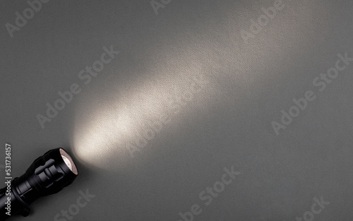 A bright beam of light from a flashlight shines on a gray background