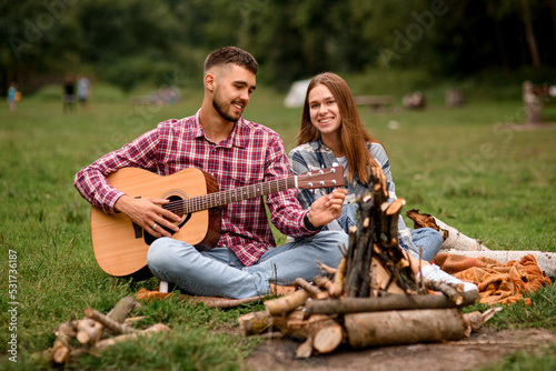 smiling couple with guitar spending time together at park. Love story. Young couple in love on romantic date at evening playing on guitar by the fire.