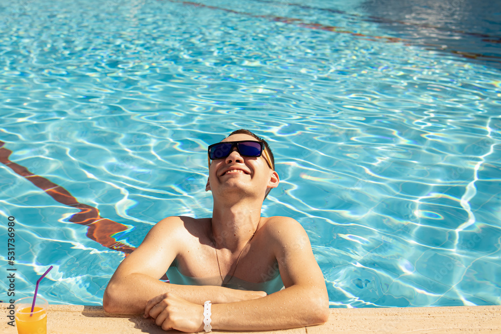 Man in sunglasses with cocktail is relaxing in the pool. Space for text. All-inclusive hotel holidays. Summer vacation. Pool party. Natural