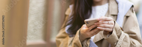 Fotografie Stylish young asian woman dressed in casual wear looking to mobile phone screen when posting photos in social media and thinking about interesting content text