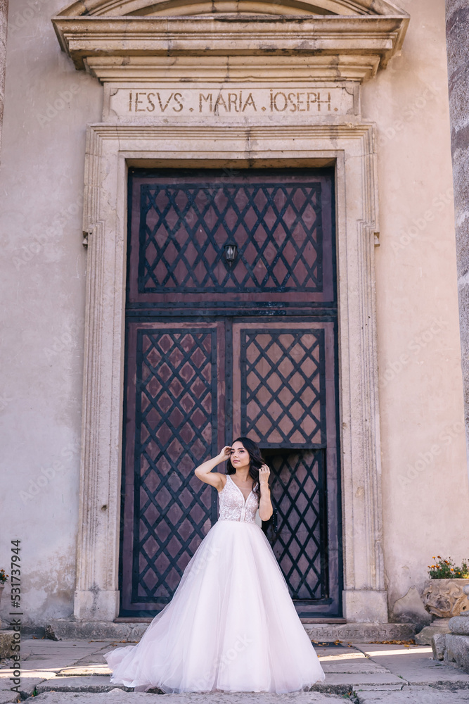 Obraz premium a bride with long black hair and a long dress stands by the black iron door at the entrance to the building.