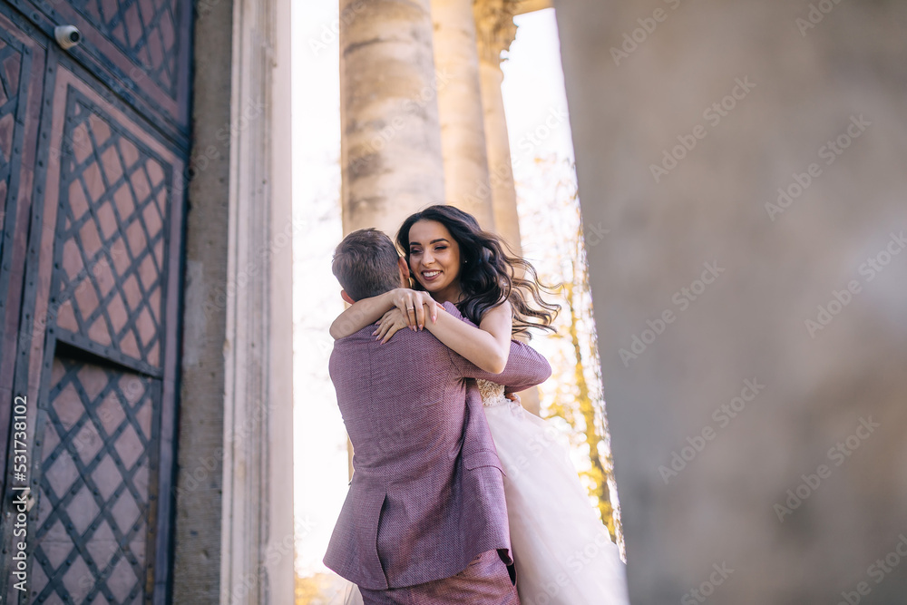 newlyweds are dancing near an old building with white columns and doors.