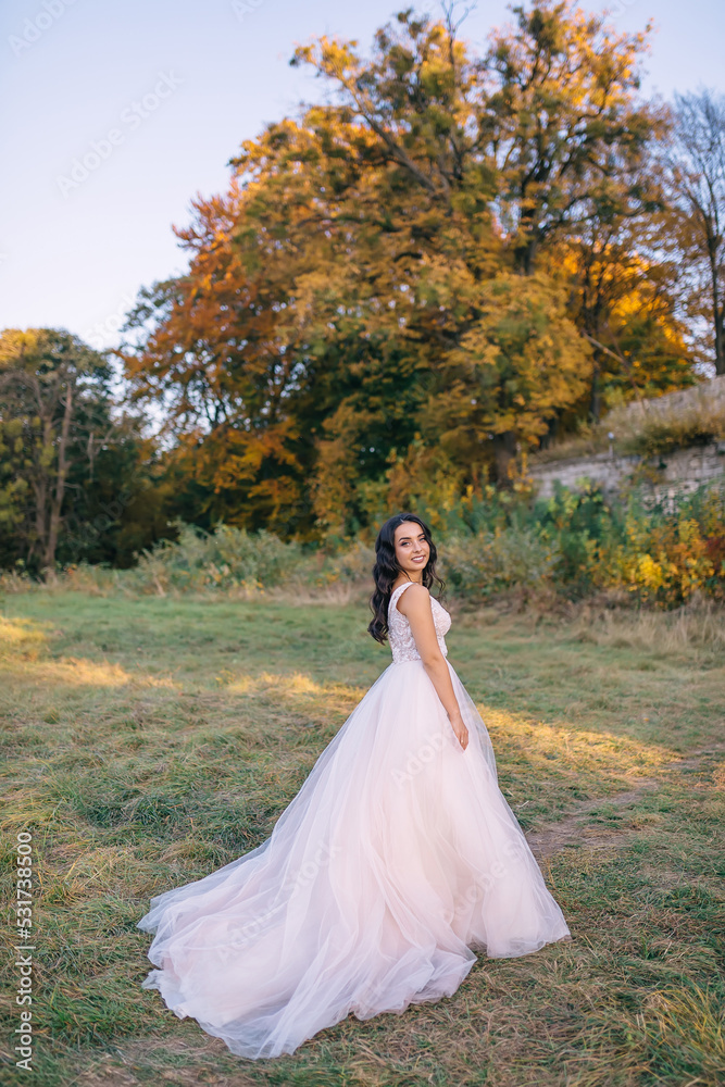 a young bride in a white dress walks in nature on her wedding day.
