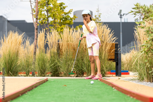 Cute preschool girl playing mini golf with family. Happy child having fun with outdoor activity. Summer sport for children and adults, outdoors. Family vacations or resort. photo