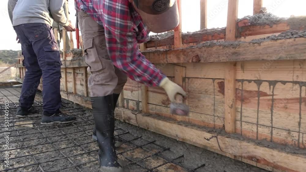 Concreting of reinforced concrete slab. Worker concretes foundation, rebar, pour cement mortar on reinforcing mesh or cage from pump concrete mixer. Builders are building a factory, hangar, house Concreting of reinforced concrete slab. Worker concretes foundation, rebar, pour cement mortar on reinforcing mesh or cage from pump concrete mixer. Builders are building a factory, hangar, house
