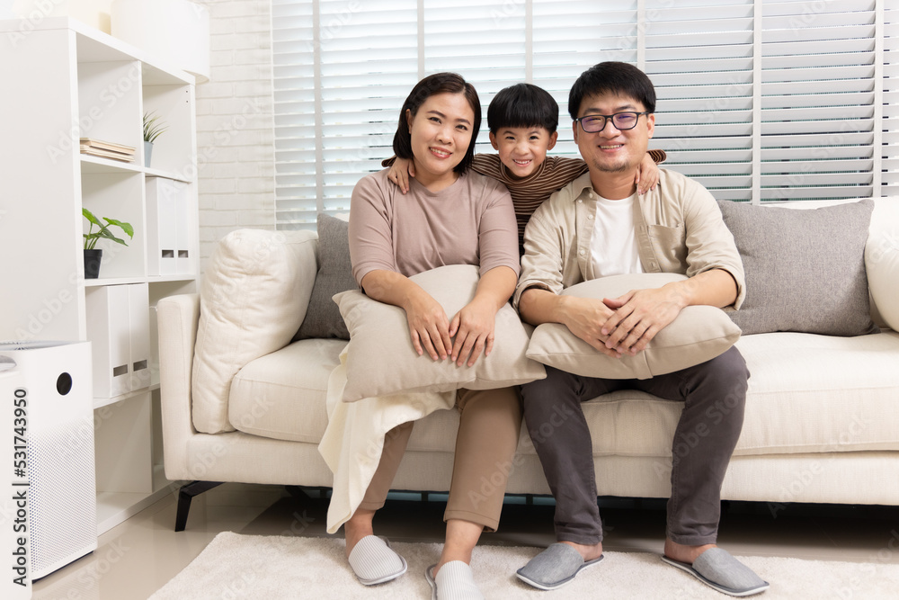 Happy Asian family with little son sitting on sofa together in living room at home Happy Asian family with little son sitting on sofa together in living room at home