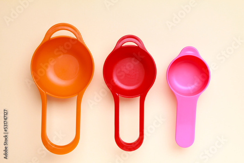 Colorful plastic measuring spoons and measuring cups on bright background top view