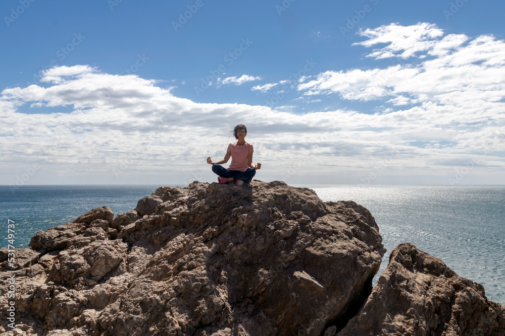 Obraz premium Woman doing yoga on a rock above the sea